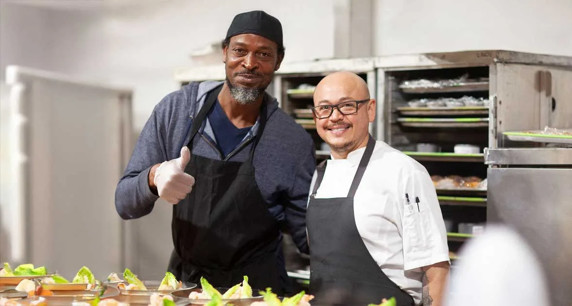 Chef and cook smiling while standing in kitchen